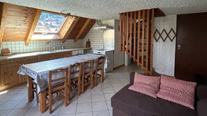 A compact kitchen with a dining area, a loft bedroom with a sloped ceiling, and a living area with a sofa.