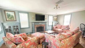 Ein Wohnzimmer mit floralen Sofas, einem Kamin, einem Fernseher und einem Deckenventilator.