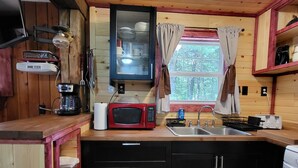 A compact kitchen with wooden cabinets, a microwave, a coffee maker, and a sink. - Green Cabin in the Woods (Irons)