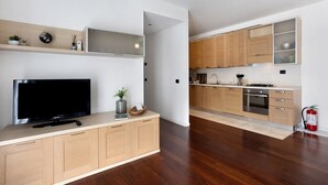 A modern kitchen with wooden cabinets, a built-in stove, and a flat-screen TV.