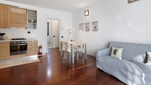 A modern kitchen with wooden cabinets, a dining table with chairs, a sofa, and a fire extinguisher.