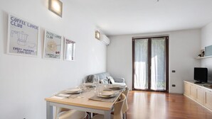 A dining area with a wooden table set for four, a sofa, and a TV on a stand.
