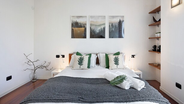 A bedroom with a bed, bedside tables, wall-mounted shelves, and artwork.