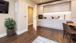 Una cocina moderna con armarios blancos, horno empotrado y comedor con mesa y sillas de madera.