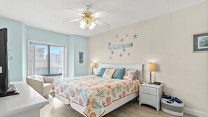 A bedroom with a bed, nightstands, a desk, a chair, a ceiling fan, and a window. - Bermuda Run 103A-2BR-Pool, Hot Tub (North Myrtle Beach)