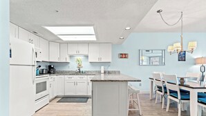 A modern kitchen with white cabinets, a granite countertop, and a dining area with a table and chairs. - Bermuda Run 103A-2BR-Pool, Hot Tub (North Myrtle Beach)