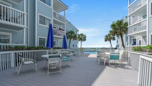 A deck with outdoor seating and a pool, surrounded by a white railing. - Ocean Garden Villas J1- 2BR/2BA- Pool (North Myrtle Beach)
