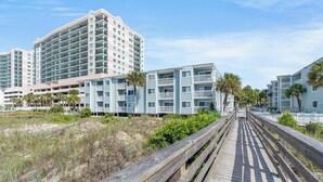 A coastal hotel with multiple-story buildings, a wooden boardwalk, and beachfront vegetation. - Ocean Garden Villas J1- 2BR/2BA- Pool (North Myrtle Beach)