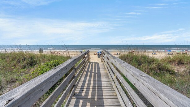 A wooden boardwalk leading to a beach with umbrellas and people in the distance. - Ocean Garden Villas J1- 2BR/2BA- Pool (North Myrtle Beach)