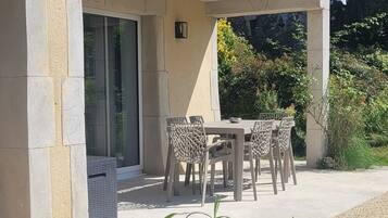 Un espace extérieur aménagé, abrité, avec une table et des chaises, une plante en pot et un bâtiment doté d’une façade en pierre et d’un balcon.