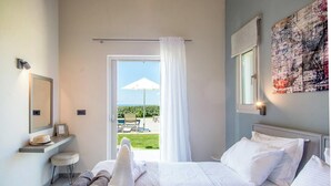 A hotel room with a bed, a desk, a chair, a small table, and a view of the outdoors.