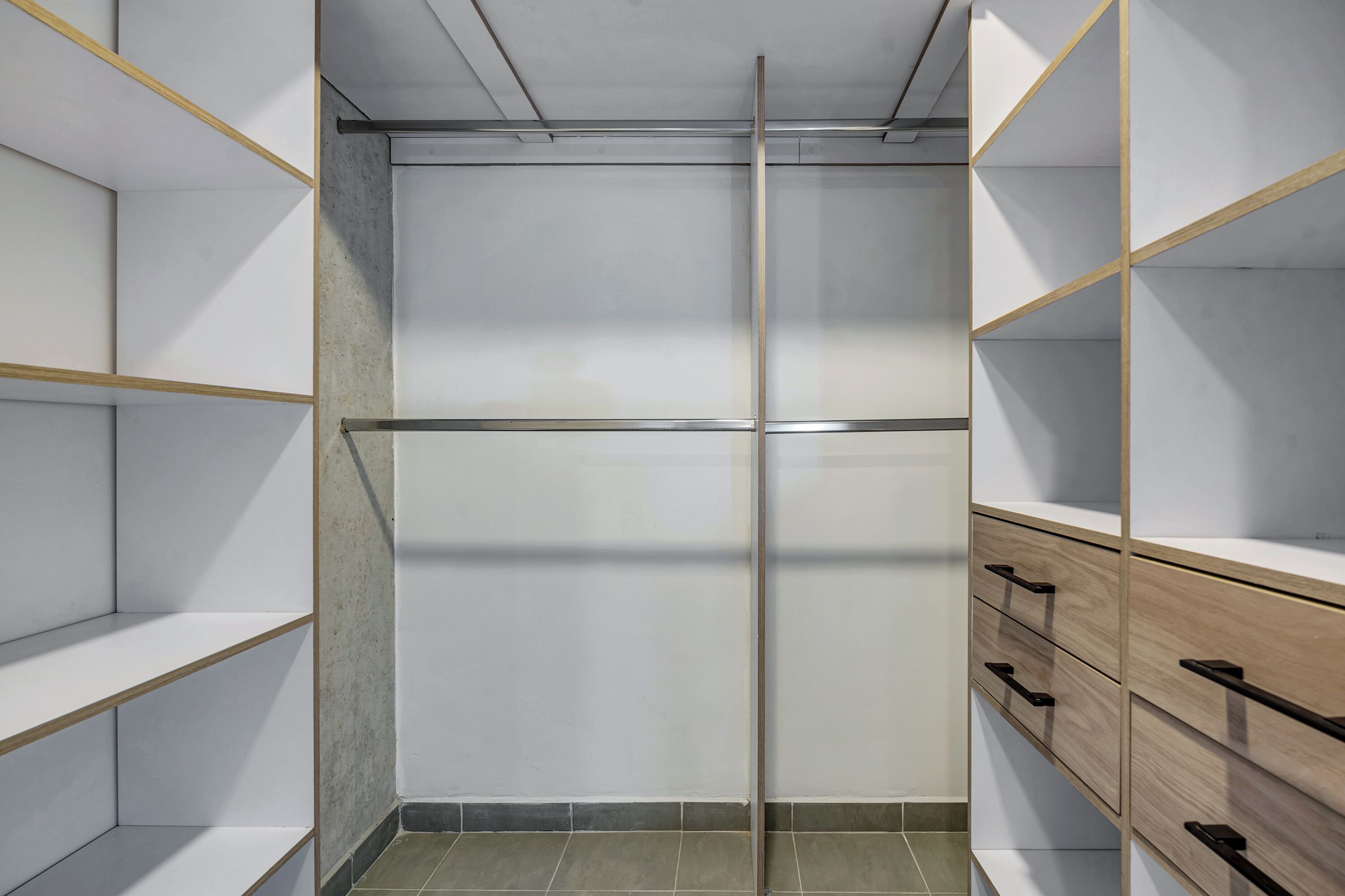 A modern, empty walk-in closet with wooden shelving and drawers.