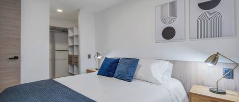 Une chambre à coucher moderne avec un grand lit, une table de chevet, une lampe de bureau et des œuvres d’art abstraites accrochées au mur.