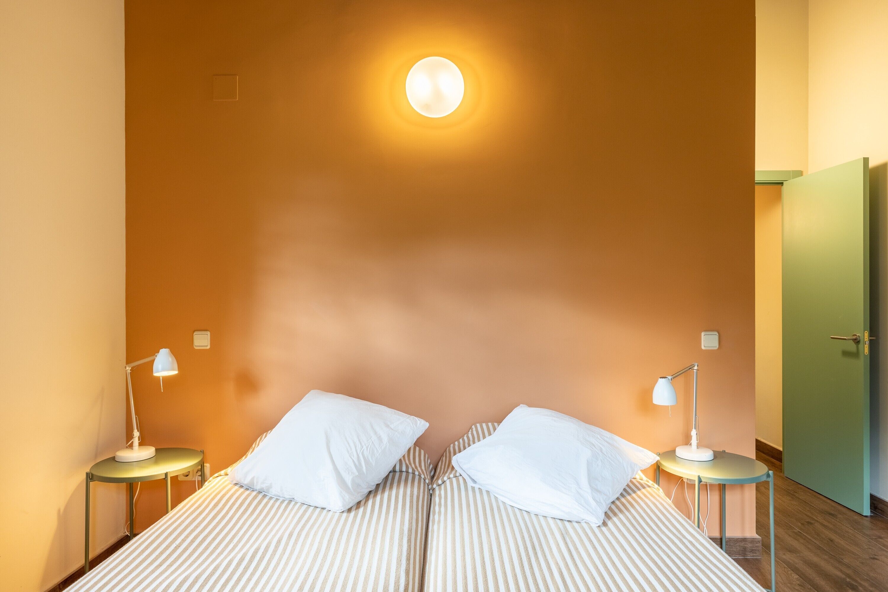 Et værelse med en seng, to sengeborde med lamper, en dør og en lampe på væggen.