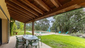 A covered patio with a pool, green chairs, and a table.
