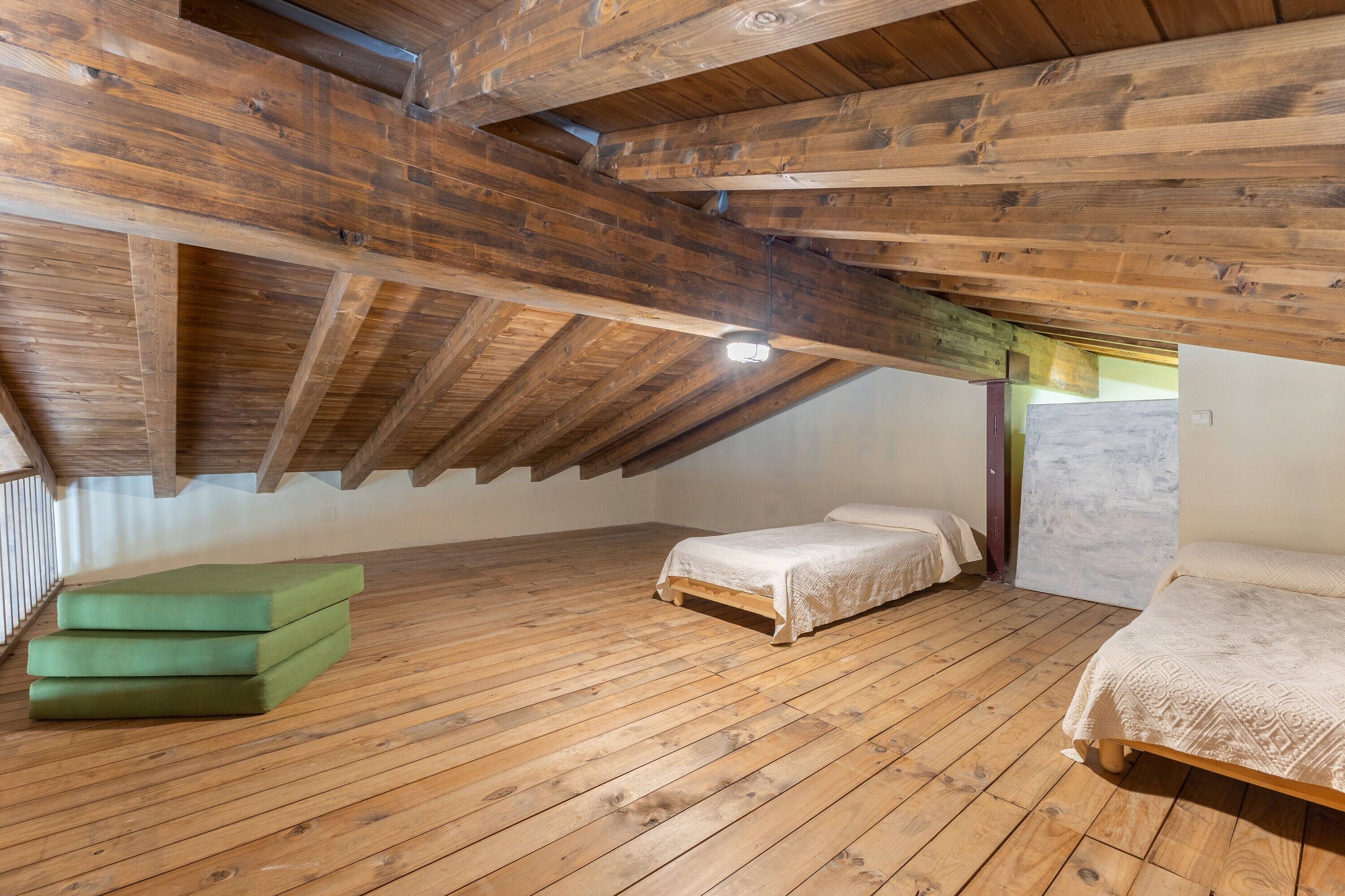 Une pièce aux hauts plafonds, avec des poutres en bois, deux lits et un banc vert.