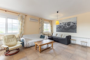 Een woonkamer met een bank, een schommelstoel, een houten salontafel en een schilderij aan de muur.