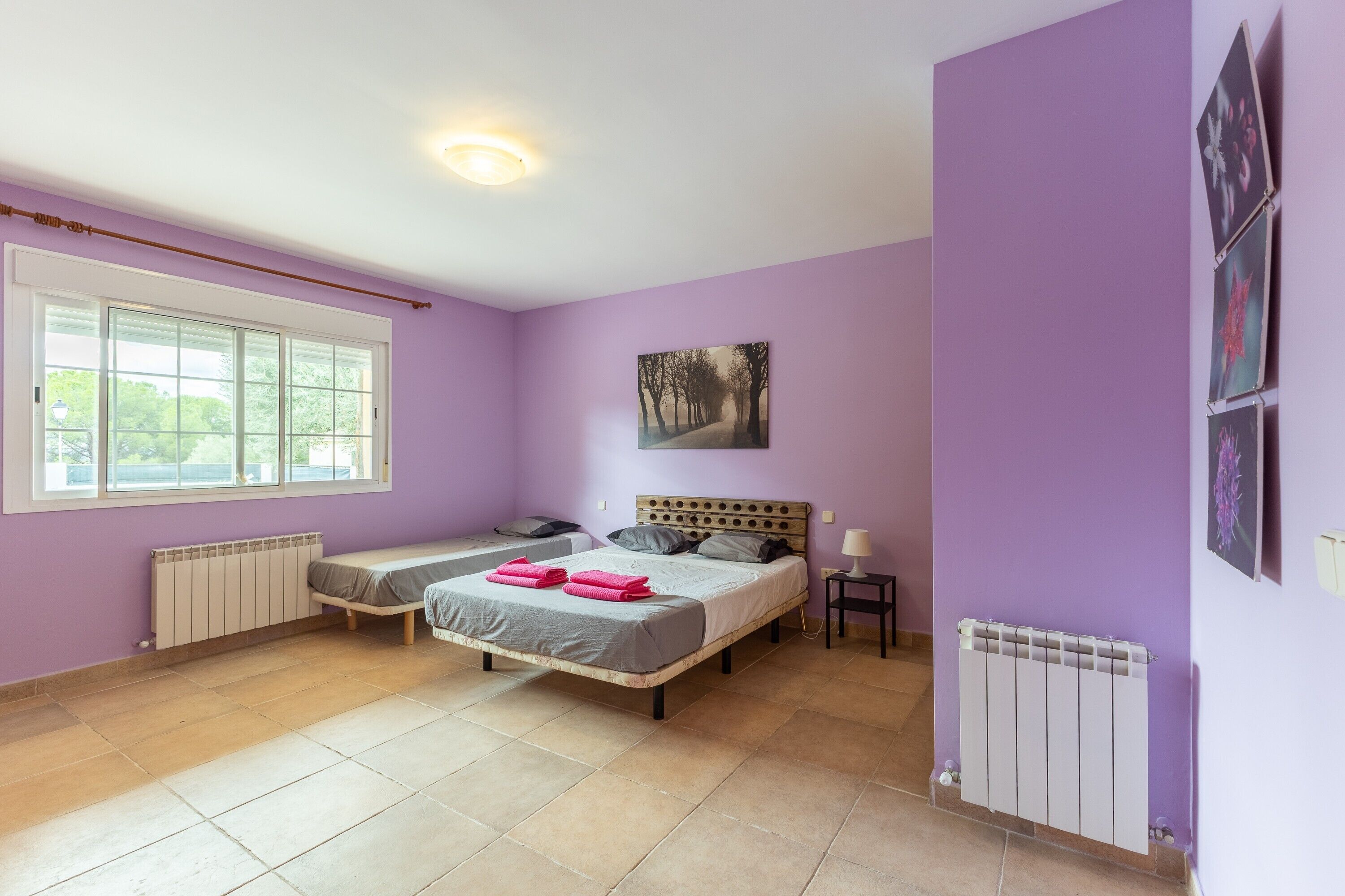 A bedroom with two beds, a window, a radiator, and a painting on the wall.