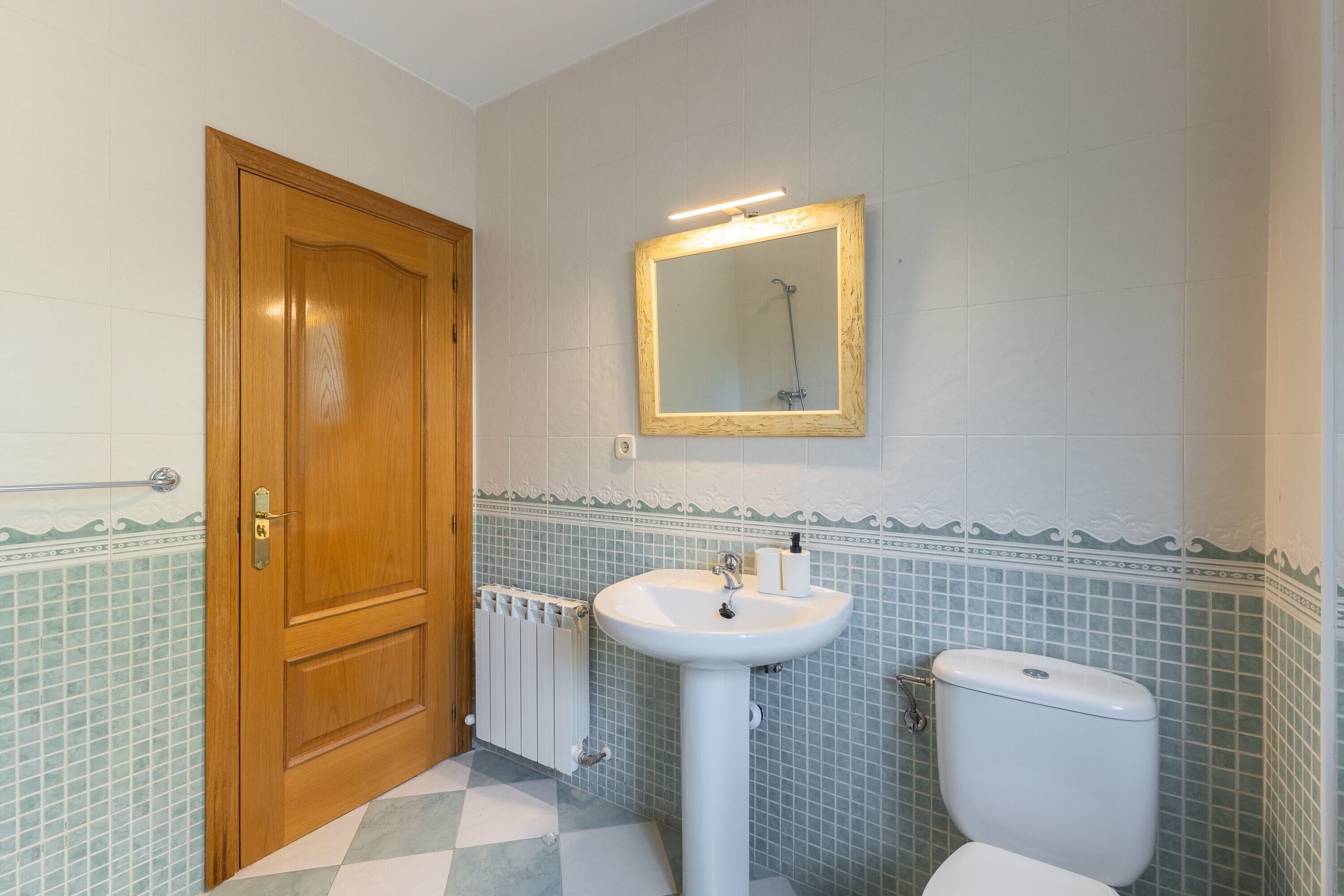 Et badeværelse med en trædør, en hvid vask, et spejl og et toilet.