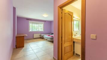 Een kamer met een bed, een houten bureau, een raam en een badkamer met een spiegel en wastafel.