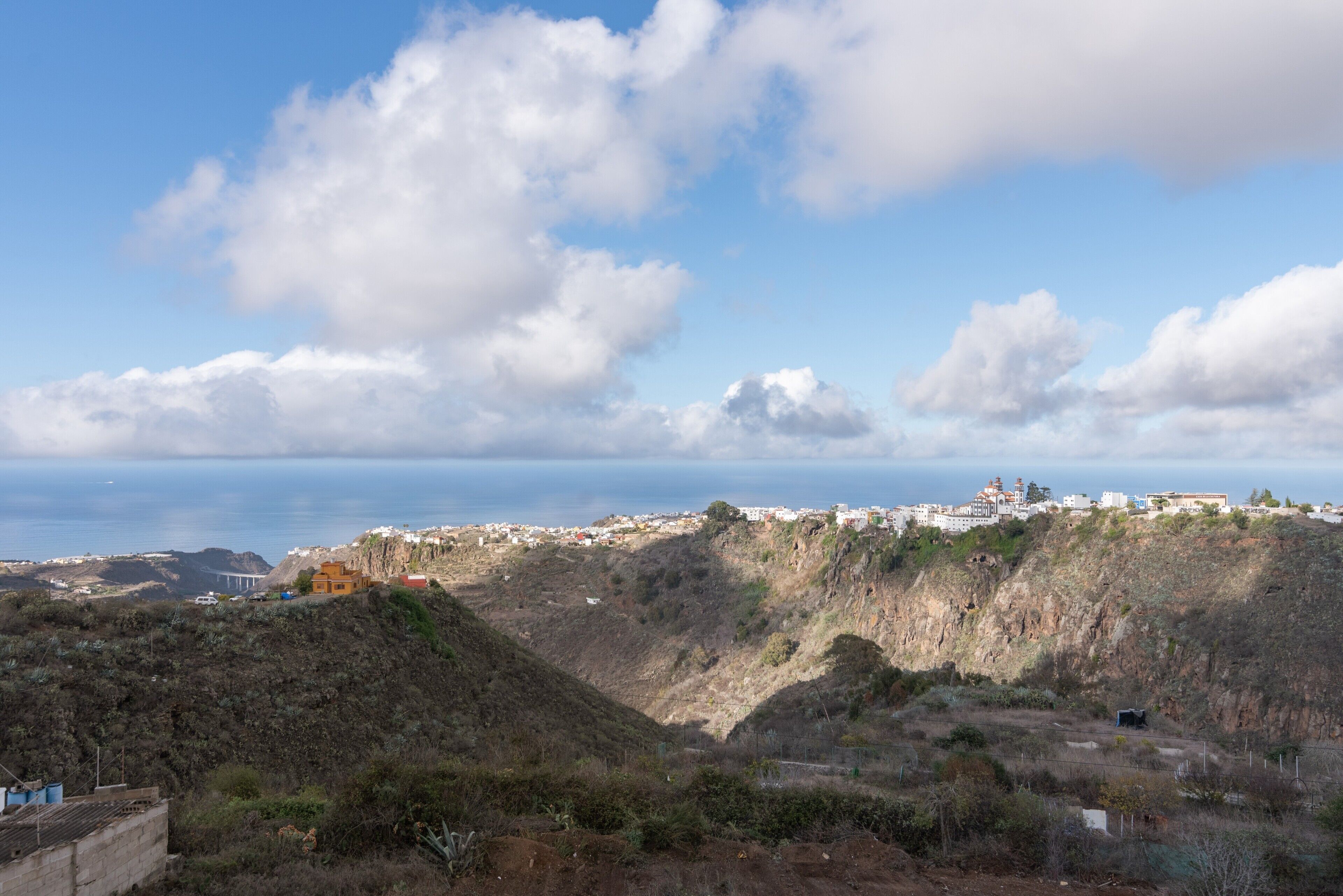 Un paisaje costero con vista al mar, una colina con edificios y un cielo despejado.