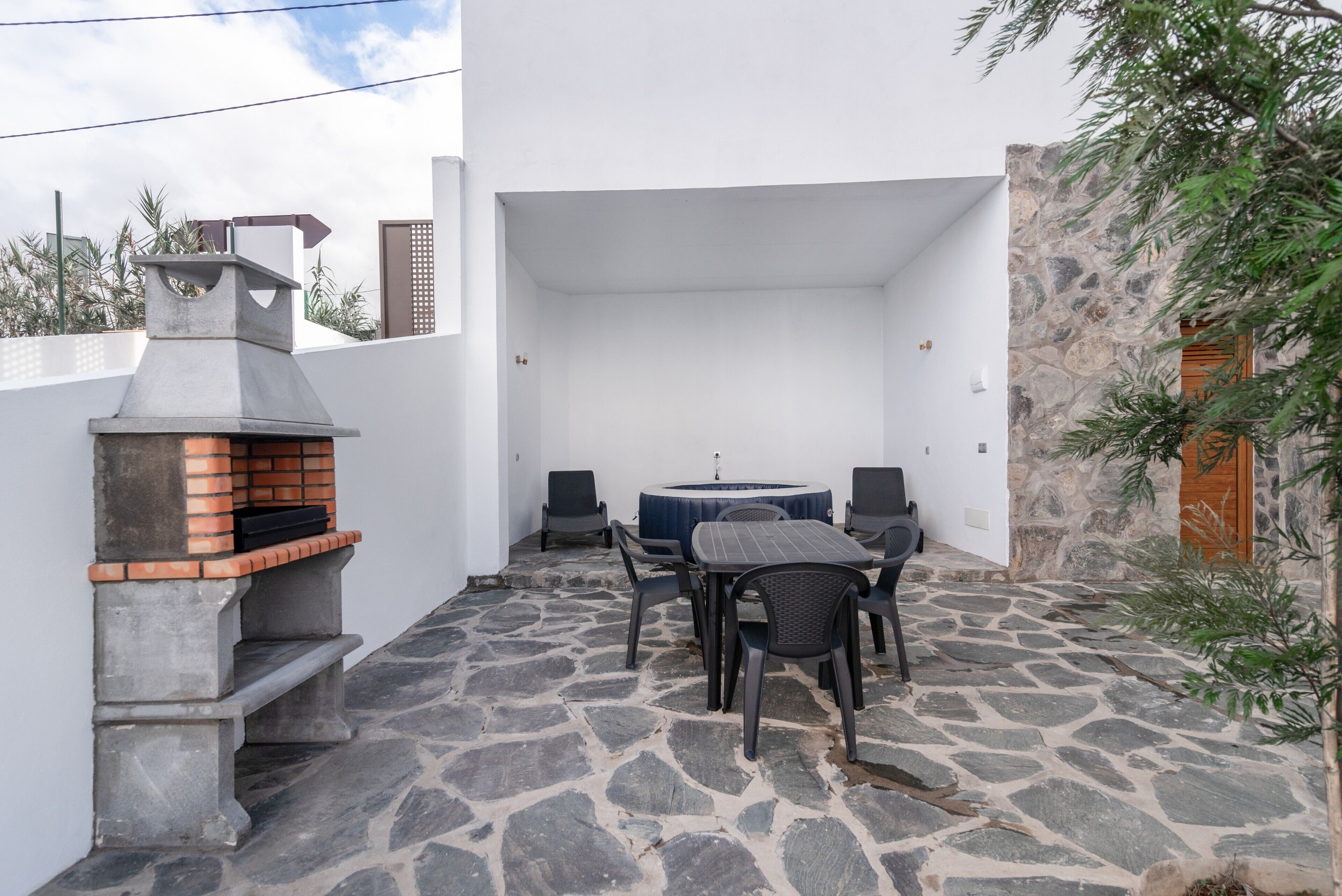 Une terrasse extérieure avec un sol en pierre, un barbecue, une table ronde avec des chaises et un mur en pierre.
