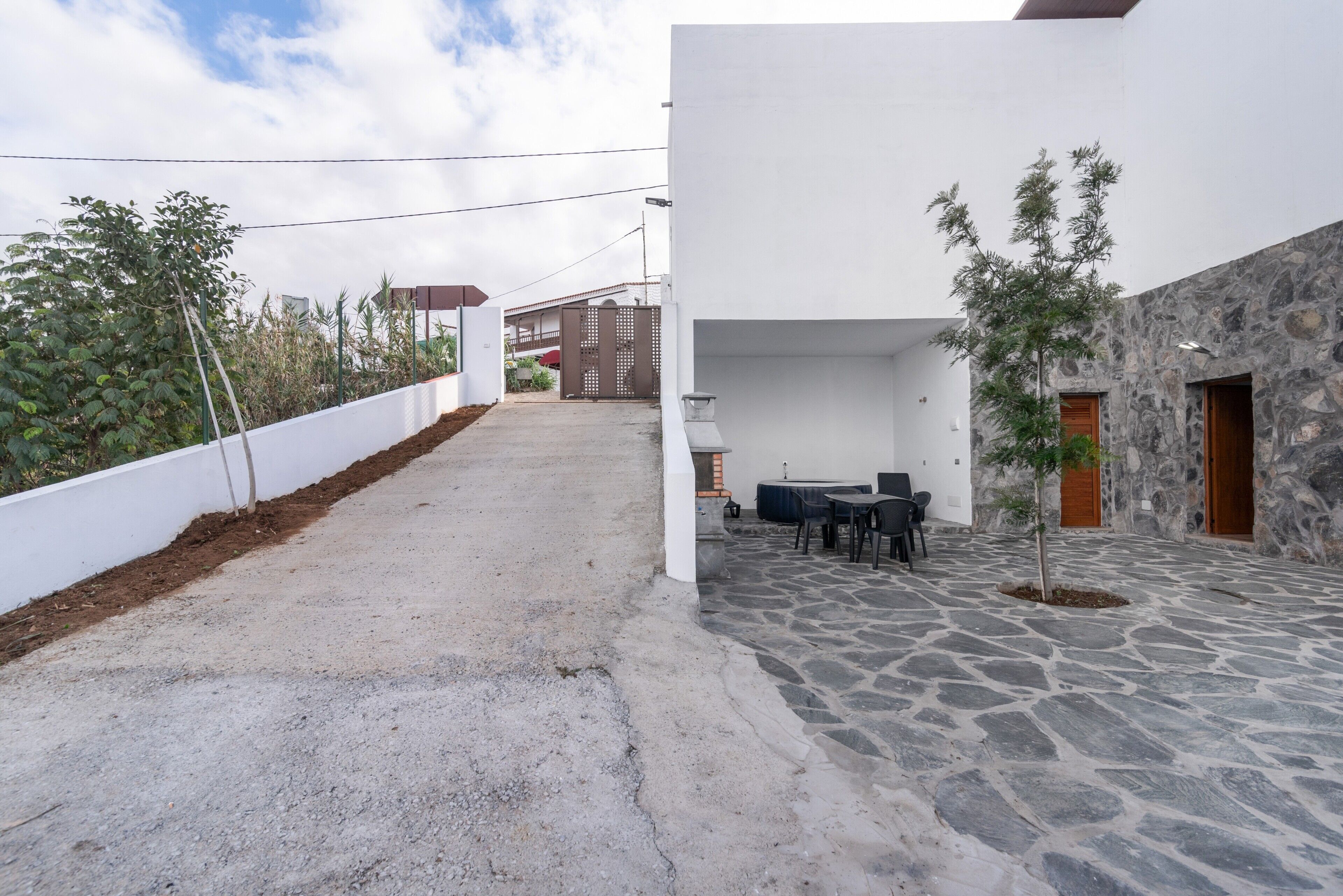 A courtyard with a stone floor, a white wall, and a small table with chairs.