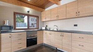 A modern kitchen with wooden cabinets, a built-in oven, and a window overlooking a backyard.