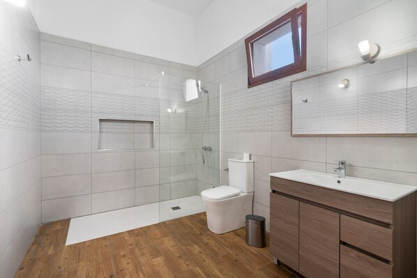A modern bathroom with a glass shower enclosure, a toilet, a sink, and a vanity with cabinets.