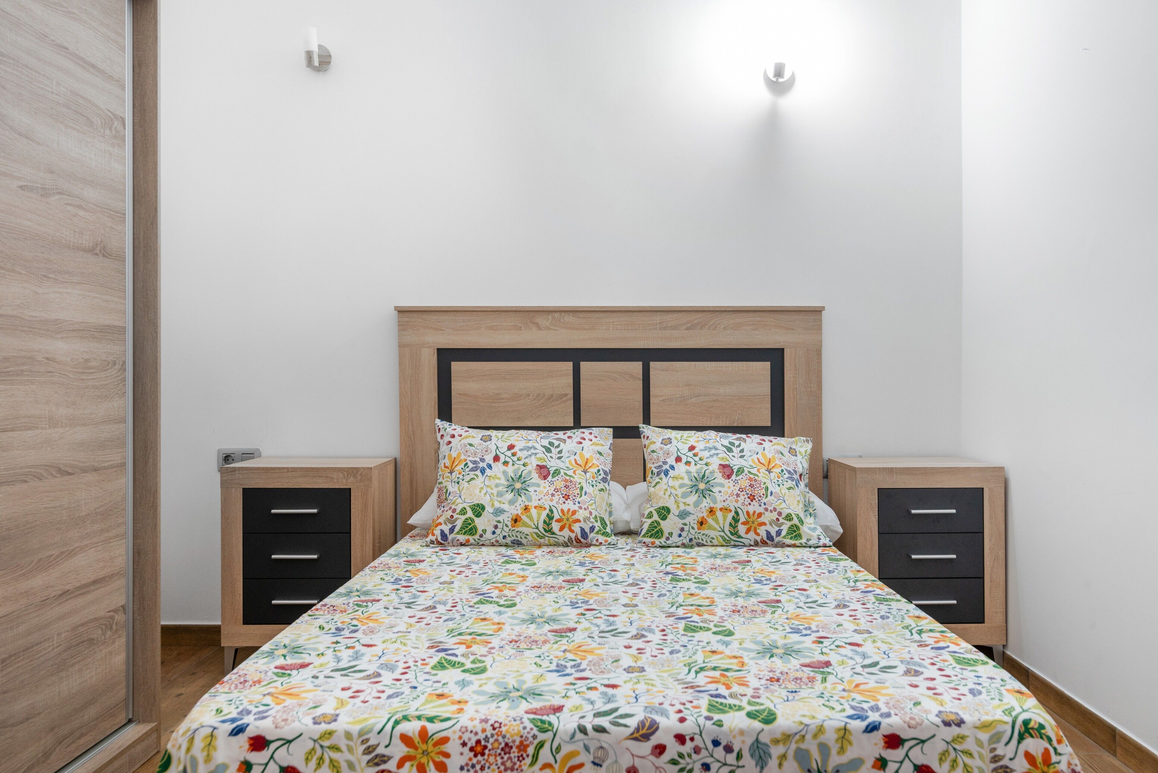 A bedroom with a wooden bed frame, two bedside tables, and a floral bedspread.