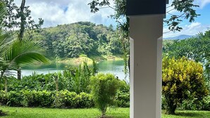 Blick auf einen üppigen Garten mit einem See, umgeben von viel Grün und einem Berg im Hintergrund.