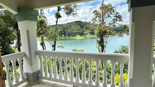 Ein Balkon mit weißer Brüstung, der auf einen von Grün umgebenen See blickt.