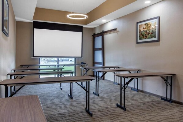 Conference room with a large projection screen and four tables, offering a view of the outdoors.