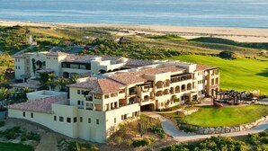 A large, multi-story resort with a central courtyard, surrounded by lush greenery and a golf course.