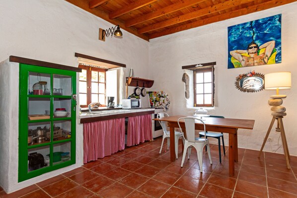 Una cocina con un mueble verde, una mesa de comedor con sillas, un microondas y un cuadro en la pared.