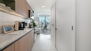 A modern kitchen with a granite countertop, wooden cabinets, and a view of the cityscape through large windows.