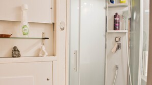 A bathroom with a glass shower enclosure, a shelf with toiletries, and a small Buddha statue.