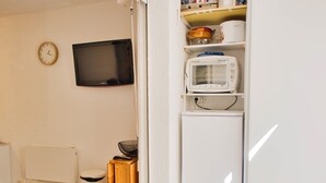 A compact kitchen with a microwave, a small refrigerator, a sink, and a toilet.