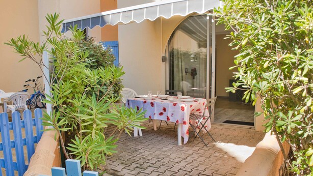A patio area with a table set for dining, surrounded by a blue fence and greenery.