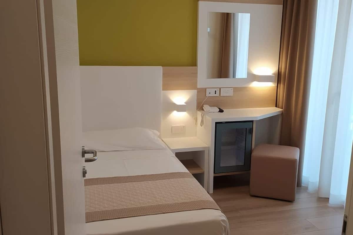 Hotelkamer met een bed, een bureau, een spiegel, een kastje en een raam met gordijnen.
