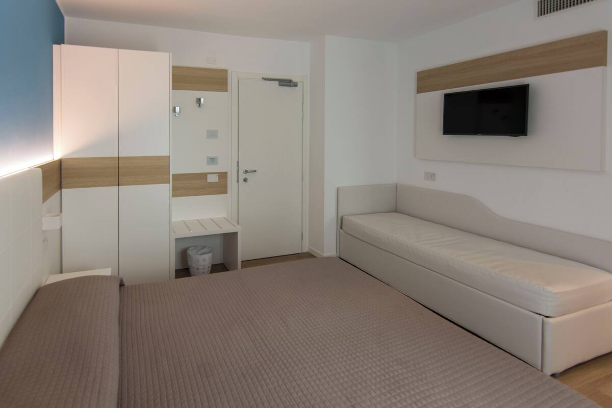 Een slaapkamer met een bed, een kledingkast, een televisie en een kleine prullenbak.