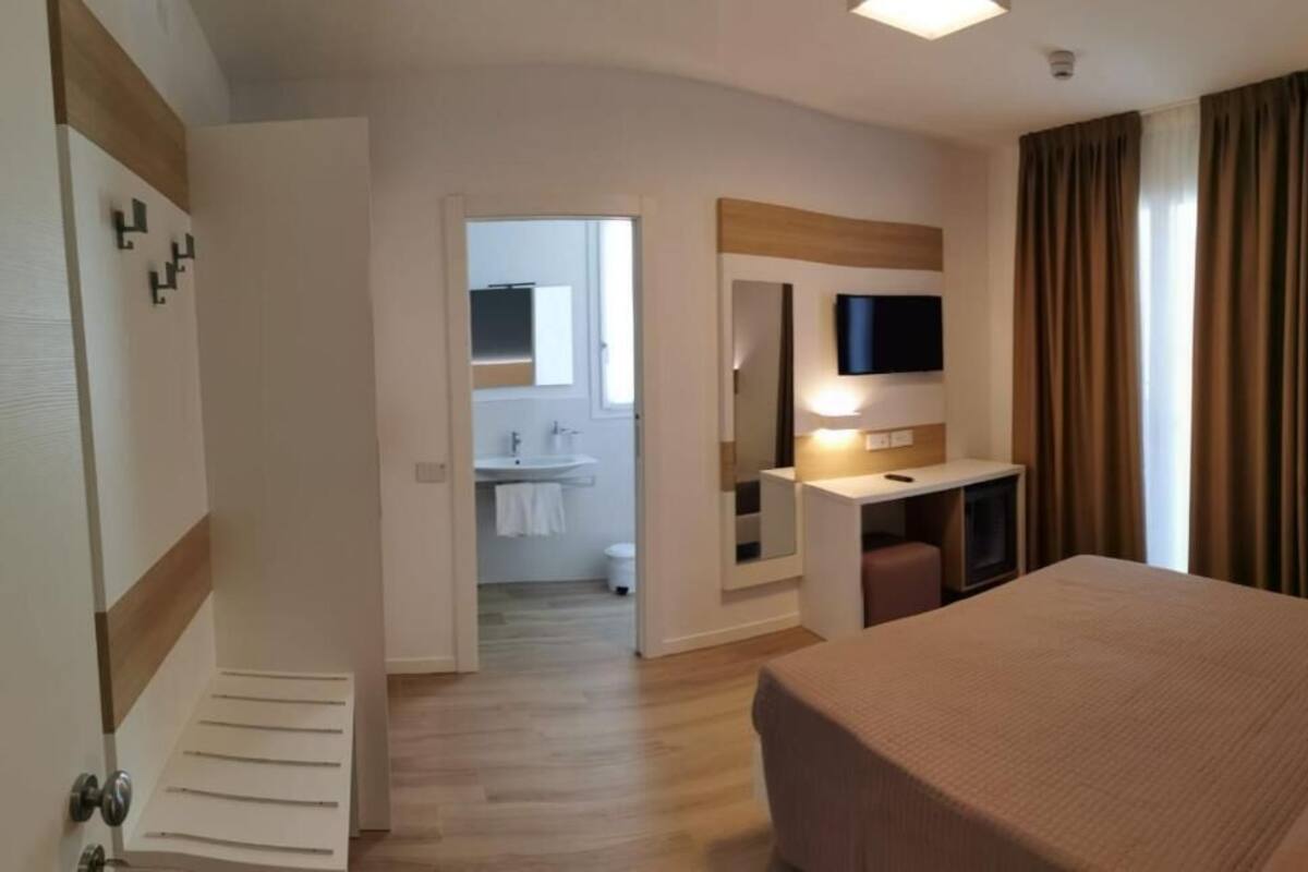 Een hotelkamer met een bed, een bureau, een televisie en een badkamer zichtbaar door een open deur.