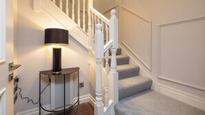 Un escalier avec des balustrades blanches et une moquette à motifs. Une lampe noire est posée sur une petite table d’appoint, à côté de l’escalier.