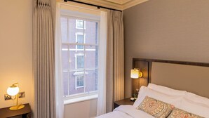 Une chambre d’hôtel avec un grand lit, un lustre, une fenêtre avec des rideaux et une table de chevet avec une lampe.