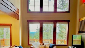 A cozy living room with a leather sofa, a fireplace, and large windows offering a view of trees. - Luxurious Home in Magical McCall (McCall)