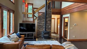 A spacious living room with a stone fireplace, leather sofas, a flat-screen TV, and a staircase leading to an upper level. - Luxurious Home in Magical McCall (McCall)