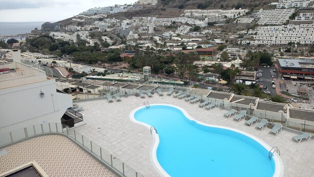 A rooftop pool with lounge chairs, a view of a coastal town, and a building with a sign 'ARIZONA'. - Vacation Home 'Las Palmeras 522 Puerto Feliz' with Sea View, Wi-Fi and Air Conditioning (Puerto Rico)