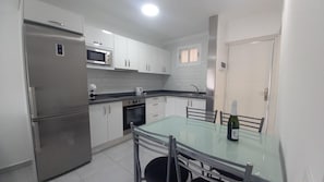 Una cocina moderna con electrodomésticos de acero inoxidable, una mesa de comedor de vidrio y armarios blancos.