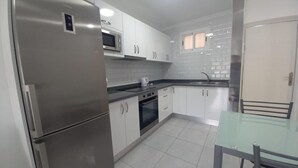 A modern kitchen with stainless steel appliances, white cabinets, a glass dining table, and a tiled backsplash. - Vacation Home 'Las Palmeras 522 Puerto Feliz' with Sea View, Wi-Fi and Air Conditioning (Puerto Rico)