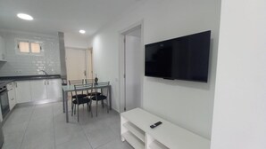 A modern kitchen with white cabinets, a dining table with chairs, a TV mounted on the wall, and a white bench. - Vacation Home 'Las Palmeras 522 Puerto Feliz' with Sea View, Wi-Fi and Air Conditioning (Puerto Rico)